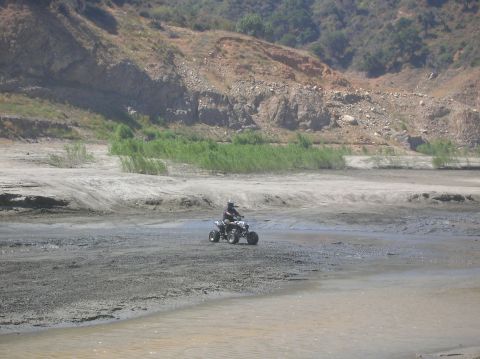 1985 Ford Bronco - A person rides a quad bike across a muddy, arid landscape with hills and sparse vegetation.