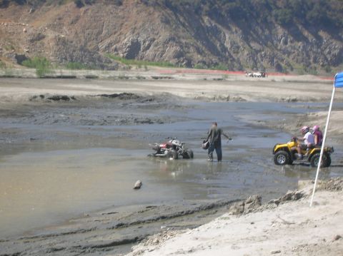 1985 Ford Bronco - ATVs navigate a muddy, off-road course with a person observing.