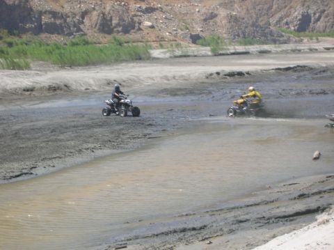 1985 Ford Bronco - ATVs navigate a challenging muddy and watery landscape under a bright sky.