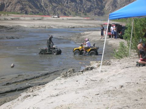 1985 Ford Bronco - ATVs navigate a muddy terrain, with spectators observing from the side.