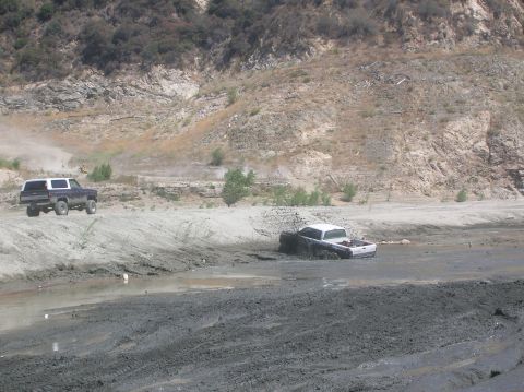 1985 Ford Bronco - Two trucks navigate a challenging off-road terrain with steep, rocky hills.