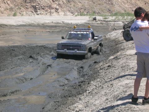 1985 Ford Bronco - Pickup truck navigating a muddy off-road course, with another vehicle in the background.