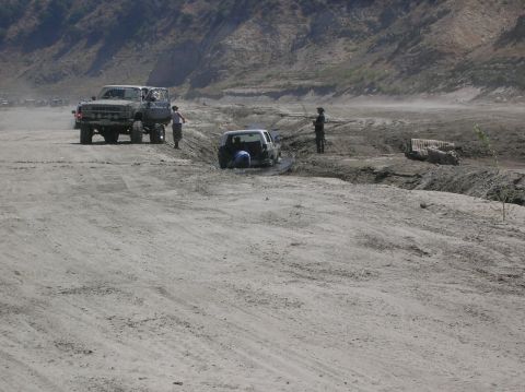 1985 Ford Bronco - Off-road vehicles navigate a challenging muddy landscape with one SUV stuck in a ditch.