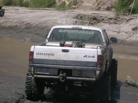 1985 Ford Bronco - A white Dodge pickup truck with "SUPER M DODGE" decal is partially submerged in mud.