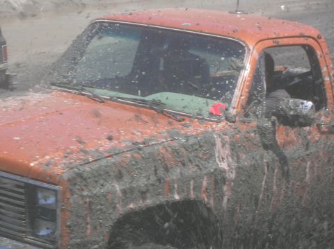 1985 Ford Bronco - Muddy orange pickup truck during an off-road event.