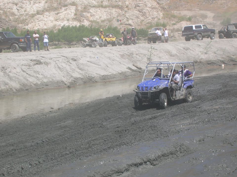 Blue UTV driving on a muddy trail with people inside