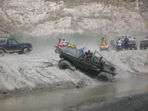 1985 Ford Bronco - Several off-road vehicles, including ATVs and modified trucks, navigate a dusty, water-filled terrain.