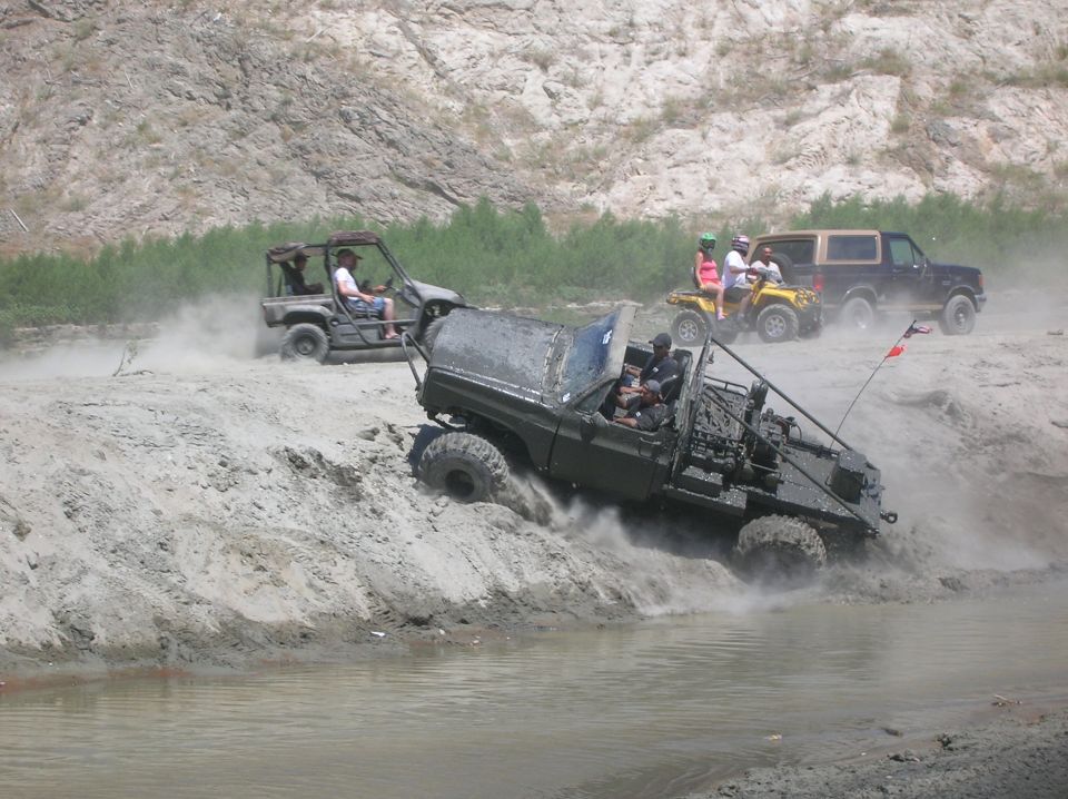 Several off-road vehicles navigate a muddy terrain with water and dust kicked up