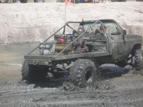 1985 Ford Bronco - Customized pickup truck with large tires navigating a muddy terrain.