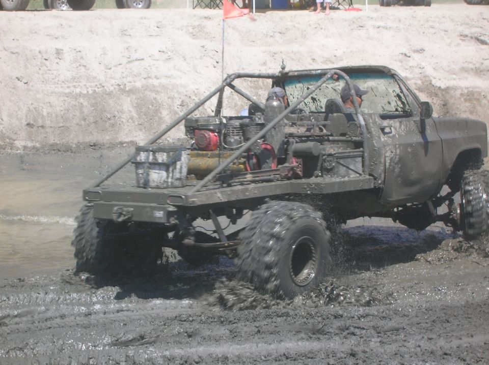 Modified pickup truck with flatbed and roll cage driving through mud