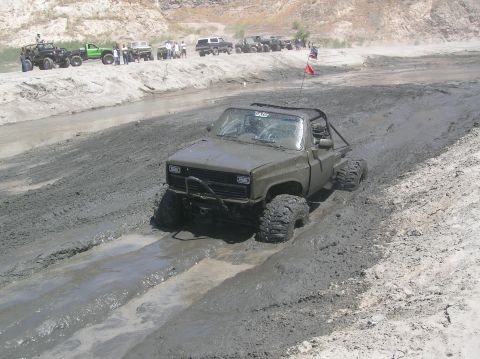1985 Ford Bronco - A heavily modified pickup truck navigates a muddy track during an off-road event.