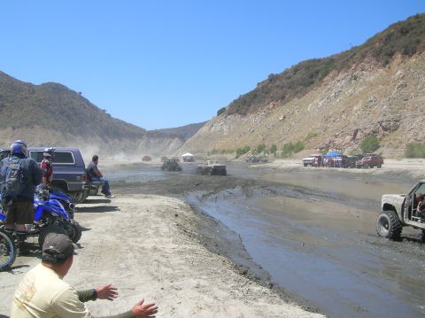 1985 Ford Bronco - Multiple off-road vehicles navigate a muddy, dusty terrain under a clear blue sky.