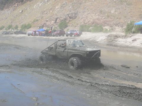 1985 Ford Bronco - A heavily modified truck navigates a muddy terrain, kicking up spray as it goes.