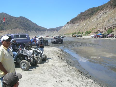 1985 Ford Bronco - Off-road vehicles and spectators gather at a muddy track on a sunny day.