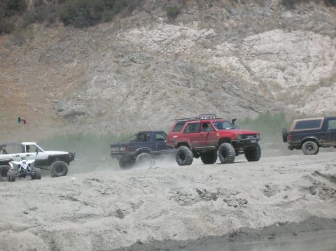 1985 Ford Bronco - Several off-road vehicles, including a black Ford Bronco, traverse a dusty, arid landscape.
