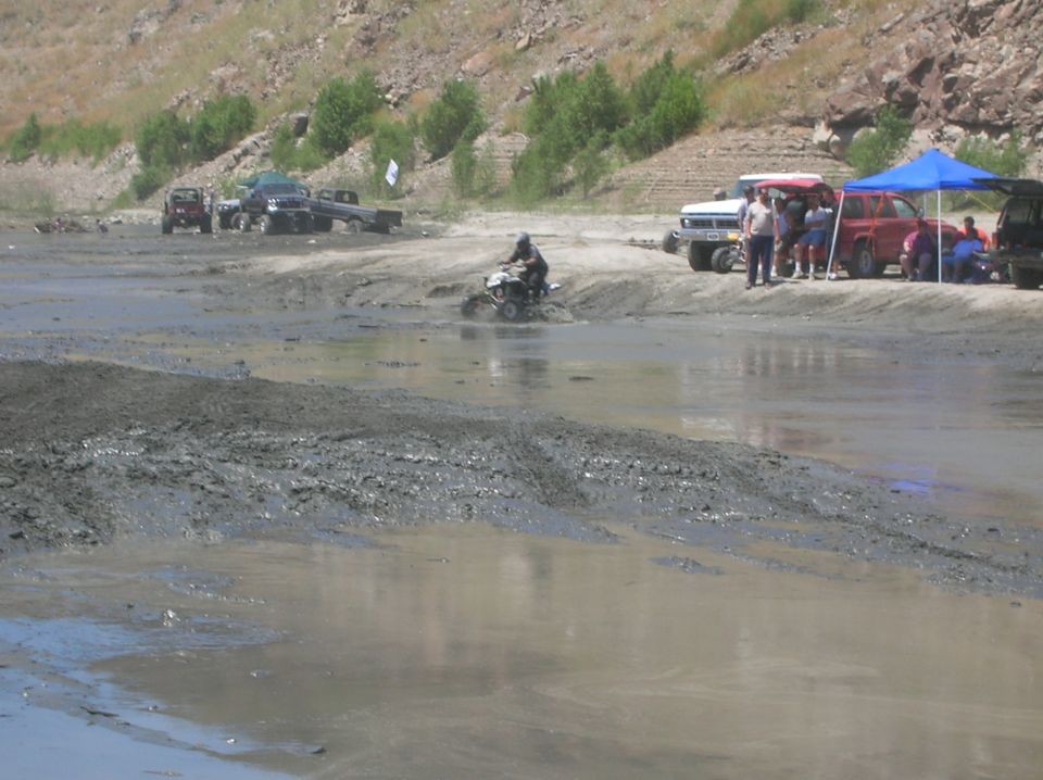ATV driving through mud with several trucks and people on the bank