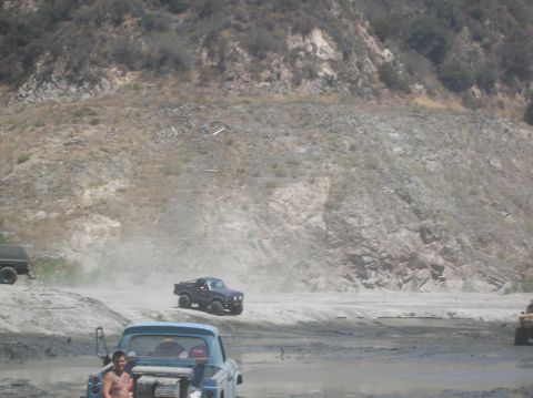 1985 Ford Bronco - Vehicles navigate a dusty off-road terrain with a mountainous backdrop.