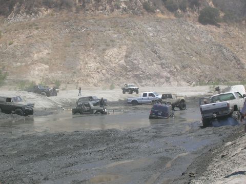 1985 Ford Bronco - Multiple off-road vehicles are stuck in the mud during an off-road event.