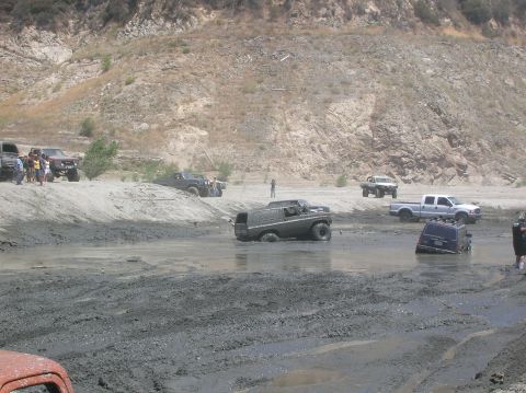 1985 Ford Bronco - Multiple vehicles are navigating a challenging muddy terrain, with some appearing to be stuck.