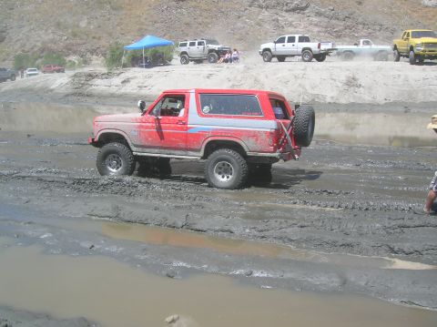 1985 Ford Bronco - A red Ford Bronco navigates a muddy off-road course, with other vehicles visible in the background.