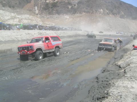 1985 Ford Bronco - Off-road vehicles navigate a muddy track, with one Bronco and another truck requiring assistance.