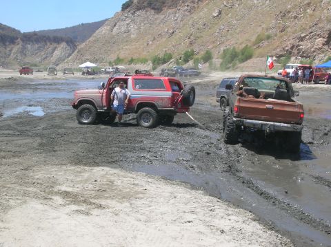 1985 Ford Bronco - Two off-road vehicles are stuck in the mud during an outdoor event.