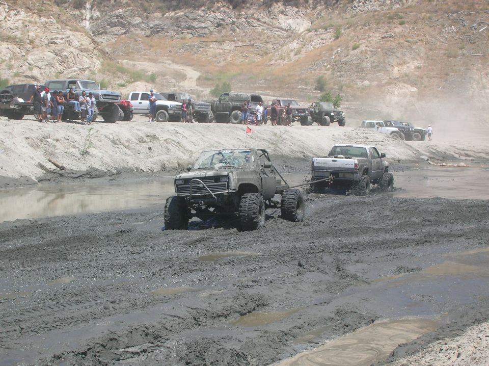 modified trucks driving through mud, one truck is being towed