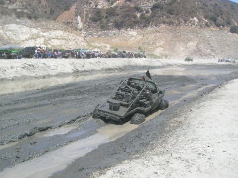 1985 Ford Bronco - Custom buggy navigates a muddy track with spectators watching from the embankment.