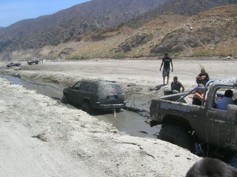 1985 Ford Bronco - Several vehicles are stuck in a muddy ditch during an off-road excursion.