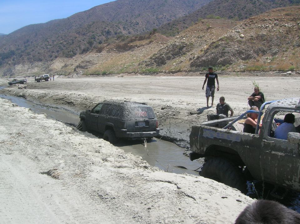 Muddy off-road vehicles stuck in a ditch with people watching