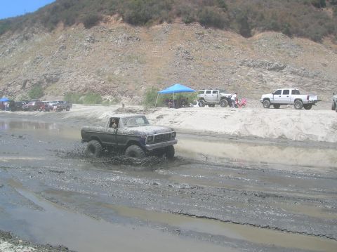1985 Ford Bronco - A Ford pickup truck navigates a muddy off-road course with other vehicles in the background.