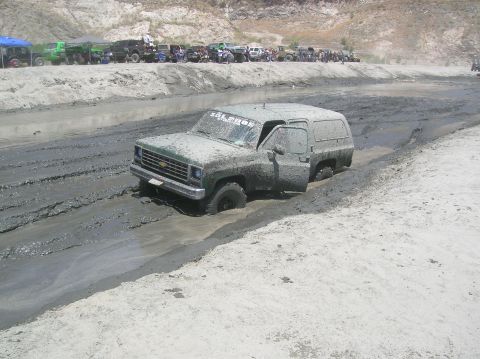 1985 Ford Bronco - Mud bogging event with a stuck SUV and spectators watching from the side.