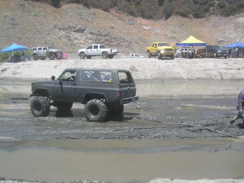 1985 Ford Bronco - Several off-road vehicles are gathered near a muddy body of water, with one vehicle appearing to be stuck.