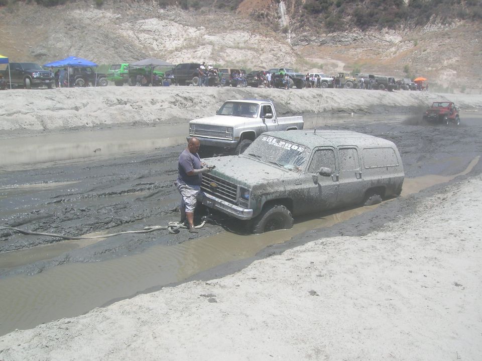 Mud-covered Chevrolet Suburban stuck in mud with a man nearby