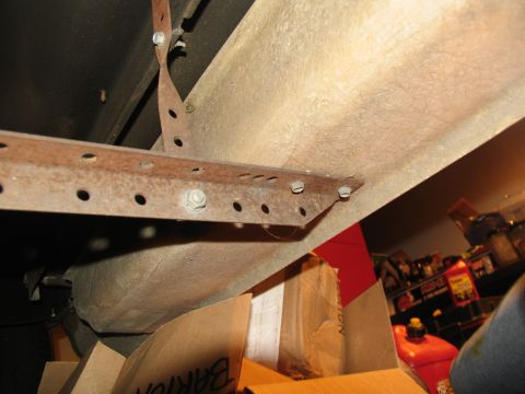 1995 Ford C-150 (Centurion Conversions) - Close-up of a rusted metal bracket with multiple bolt holes, attached to the underside of a vehicle. Boxes and a red gas can are visible in…