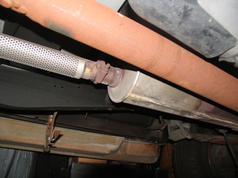 1995 Ford C-150 (Centurion Conversions) - Close-up of the rusted exhaust system components on the underside of a vehicle.