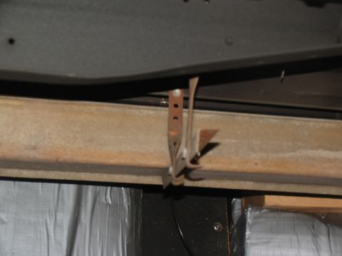 1995 Ford C-150 (Centurion Conversions) - A close-up view of a rusty metal bracket, possibly for a running board, attached to the underside of a vehicle.