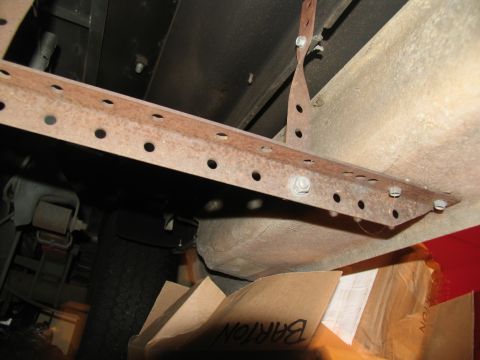 1995 Ford C-150 (Centurion Conversions) - The rusted metal bracket shows numerous holes for mounting, with a tire and boxes visible beneath the vehicle.