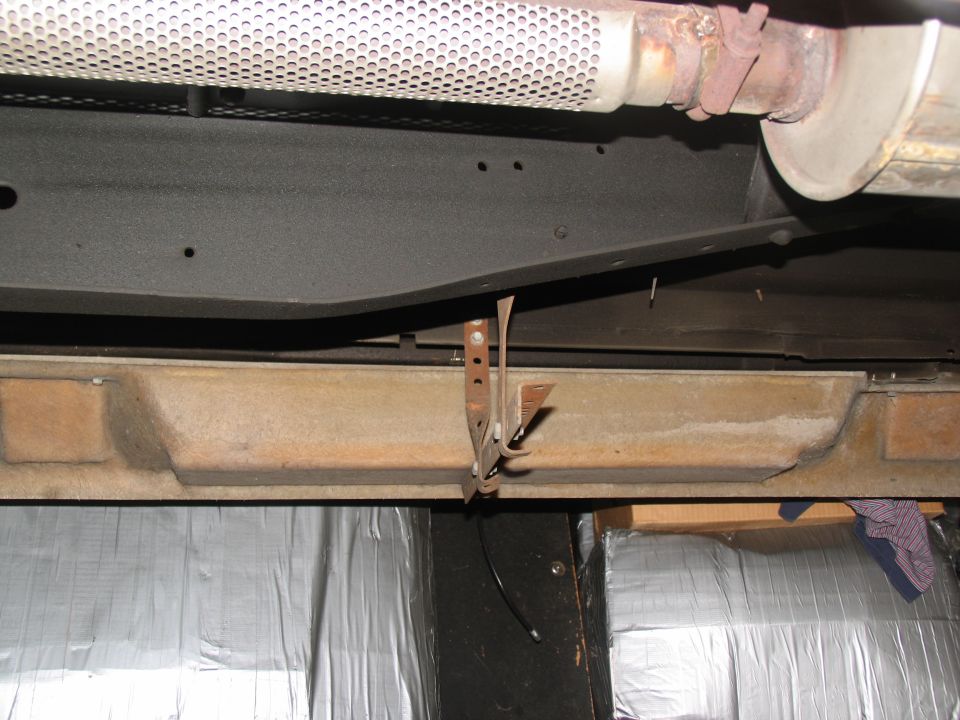 Underside view of a vehicle frame with exhaust pipe and a rusty bracket attached