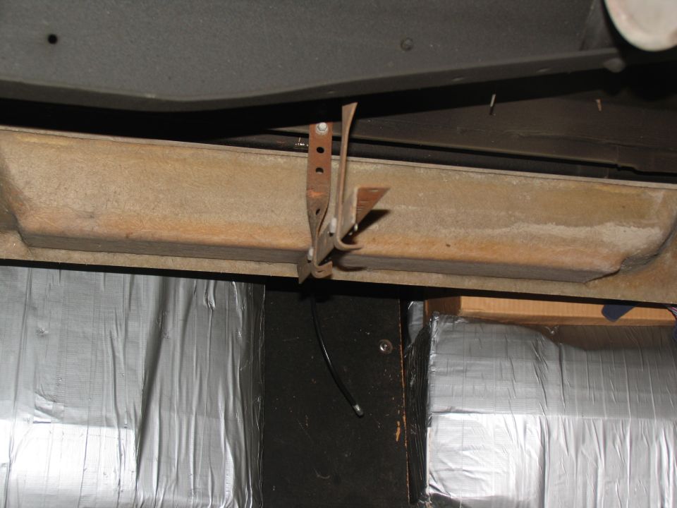 Rusty metal bracket attached to a vehicle's undercarriage, with silver insulation visible below