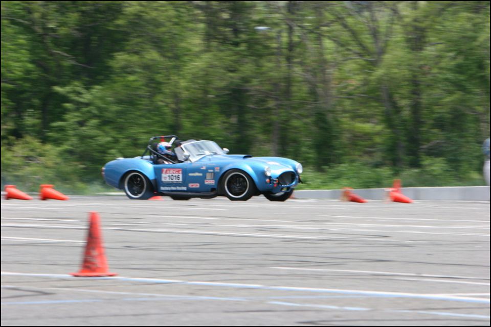 Blue sports car with racing decals navigates an autocross course with orange cones
