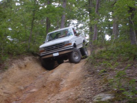 1992 Ford Bronco - A 1992 Ford Bronco navigates a challenging off-road trail with steep inclines and dense trees.