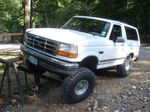 1992 Ford Bronco - A white 1992 Ford Bronco is positioned on a metal ramp, its off-road tires and front grille.