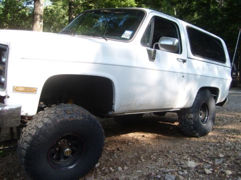 1992 Ford Bronco - White SUV with lifted suspension and off-road tires is parked outdoors on a gravel surface.
