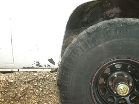 1992 Ford Bronco - The vehicle's white paint is chipped, revealing rust around the wheel well and lower body panel.