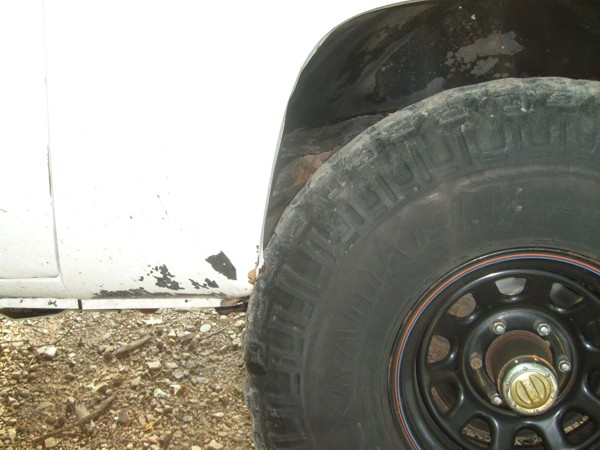 Close-up of a tire and wheel well on a white vehicle. Some rust is visible