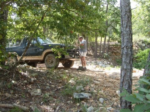 1992 Ford Bronco - A man inspects his Ford Bronco on a rough, wooded path.