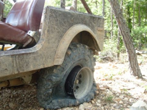 1992 Ford Bronco - A flat tire on a Jeep CJ-7, seen off-road with its brown interior visible.