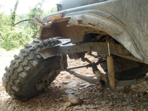 1992 Ford Bronco - The front fender and suspension of this vehicle are heavily damaged, revealing large off-road tires and a rough terrain.