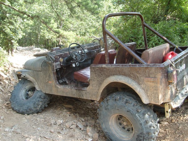Jeep CJ-7 with roll cage and large tires on a rocky trail. Red gas can in the back